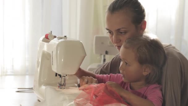 Молодая привлекательная мать работает над швейной машинкой со своей маленькой милой дочкой — стоковое видео