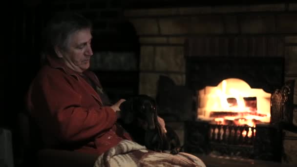 Старик ласкает собаку у камина — стоковое видео