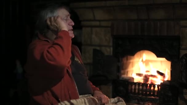 Пожилой человек говорит по телефону сидя на стуле перед камином — стоковое видео