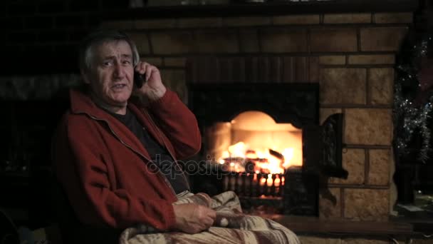 Senior man speaking by mobile phone sitting in front of the fireplace — Stock Video © Alexeg84 #153256488 Download royalty-free Senior man speaking by mobile phone sitting in the chair in front of the fireplace. Burning firewood warming dark room stock video 153256488 from Depositphotos collection of millions of premium high-resolution stock photos