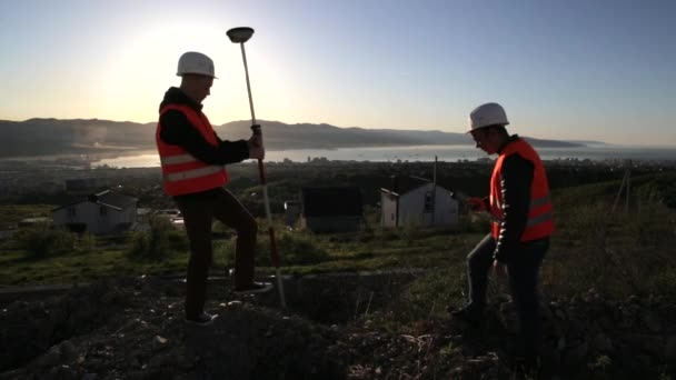 Zwei Vermessungsingenieure in Helmen, die auf dem Gipfel des Berges geodätische Messungen durchführen — Stockvideo