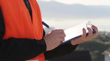 Caucasion adam turuncu yelek bir tablet için bağlı kağıt üzerinde veri yazma