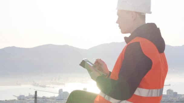 Landmeter in de helm en oranje vest perfoming metingen buiten zitten — Stockvideo