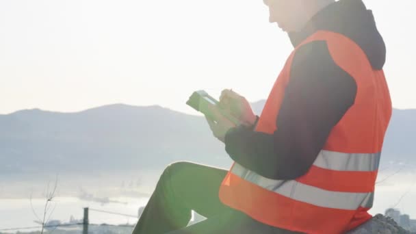 Junger Arbeiter, der geodätische Messungen im Freien durchführt. gegen die Sonne geschossen — Stockvideo