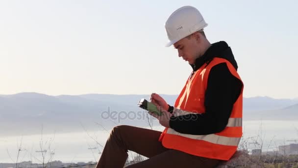 Knappe mannelijke ingenieur in vest en helm zittend op zijn buiten werkplek — Stockvideo