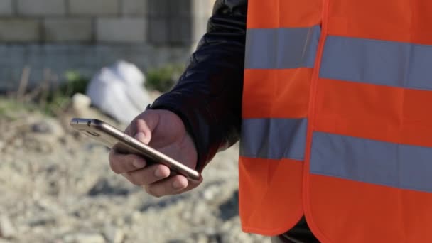 Imagem cortada do trabalhador em colete usando telefone inteligente no local de trabalho ao ar livre — Vídeo de Stock