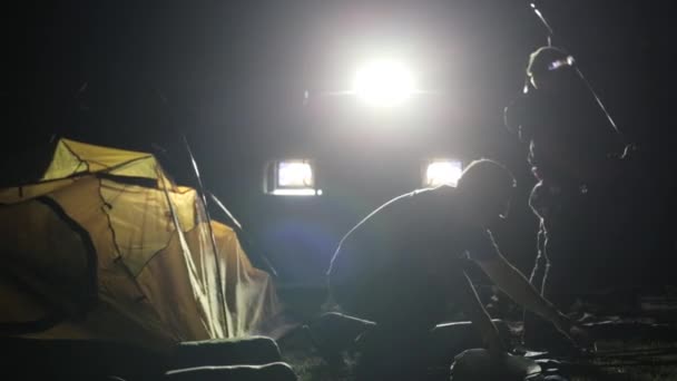 Disparo nocturno de dos hombres adultos y un niño erigiendo tienda en ligh de SUV . — Vídeos de Stock