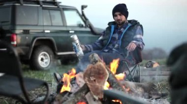 Oduncu stil kamp ateşi oturan erkek seyahat kılığında.