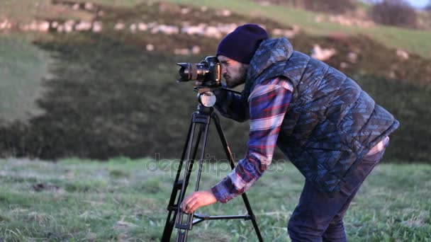 Молодой фотограф, работающий на природе с камерой и штативом — стоковое видео