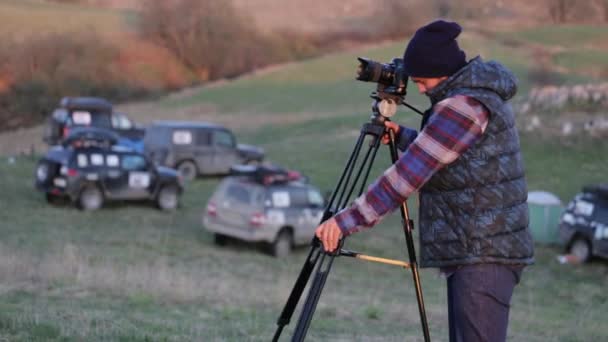 Молодий фотограф працює на природі з фотоапаратом і штативом — стокове відео