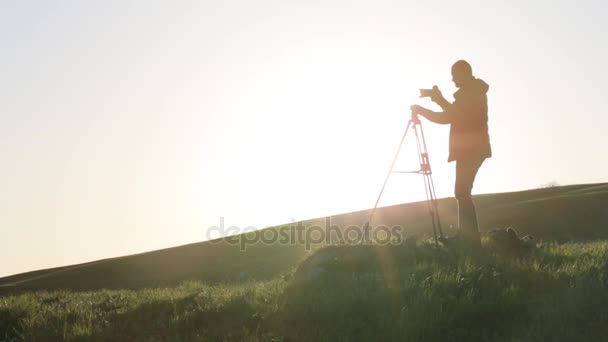 Fotograaf opent statief mechanisme en camera ingesteld op top van de groene heuvel. — Stockvideo