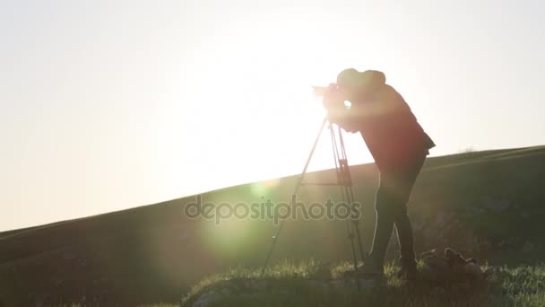 A fotós, lövés a fényképezőgép és az állványt a domb tetején. — Stock videók