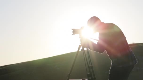 O fotógrafo atirando com câmera e tripé no topo da colina . — Vídeo de Stock