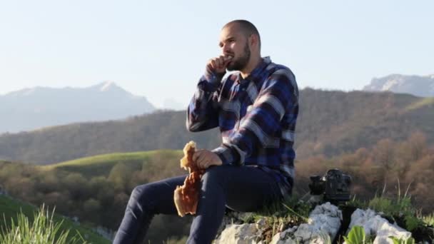 Лысый, красивый мужчина в природе ест хлеб на прекрасном горном ландшафте . — стоковое видео
