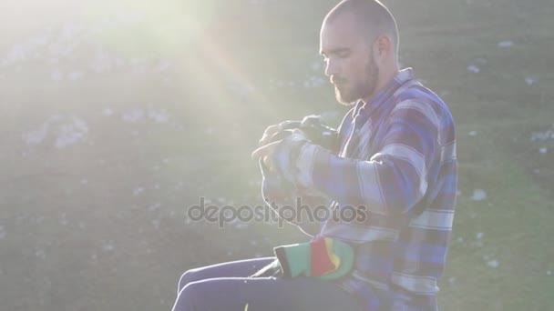 Fotógrafo sentado y cambiando lentes en cámara profesional al aire libre . — Vídeo de stock