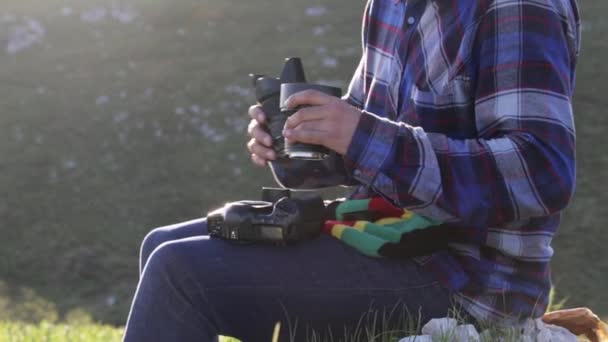Fotógrafo sentado y cambiando lentes en cámara profesional al aire libre . — Vídeos de Stock