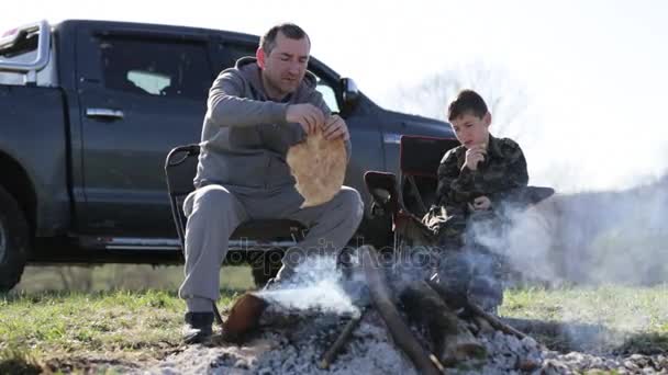 Сім'я батька і сина їсть смажений хліб поруч з багаттям — стокове відео
