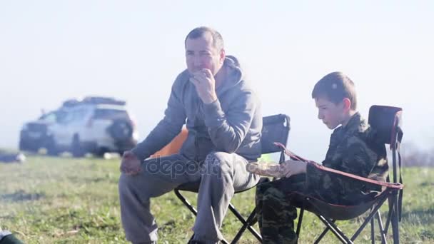 아버지와 캠프 파이어 옆에 구운된 빵을 먹는 아들의 가족 — 비디오