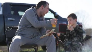 Baba ve oğul kamp ateşi yanında kızarmış ekmek ve içecek soda yeme