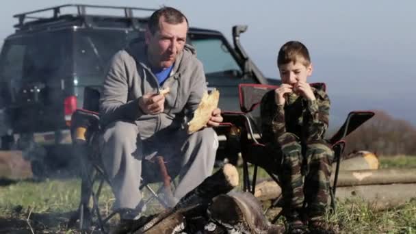 Vader en zoon eten geroosterde brood en drinken frisdrank naast kampvuur — Stockvideo
