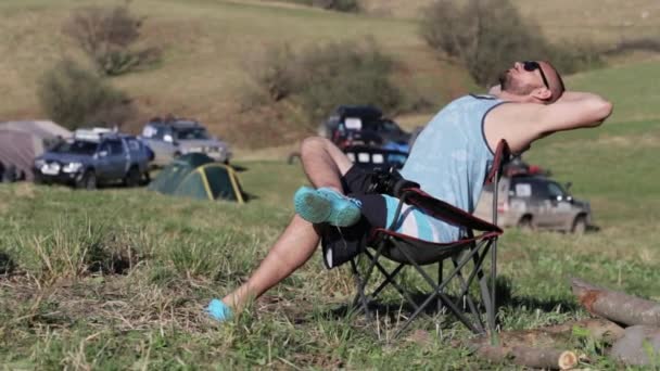Hombre sentado en la silla y estirándose en el campamento expedicionario . — Vídeo de stock