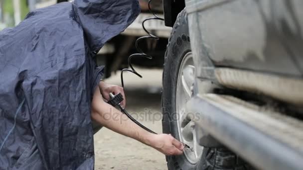 Человек в плаще накачивает колеса внедорожника на обочине дороги — стоковое видео
