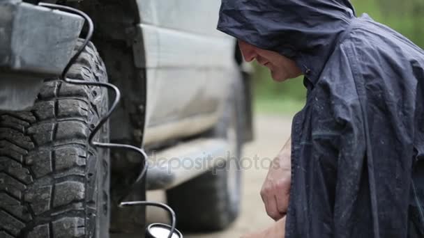Ο άνθρωπος σε αδιάβροχο άντληση τροχούς του Suv στην άκρη του δρόμου — Αρχείο Βίντεο