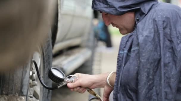 Людина в плащі накачує колеса позашляховика на узбіччі — стокове відео