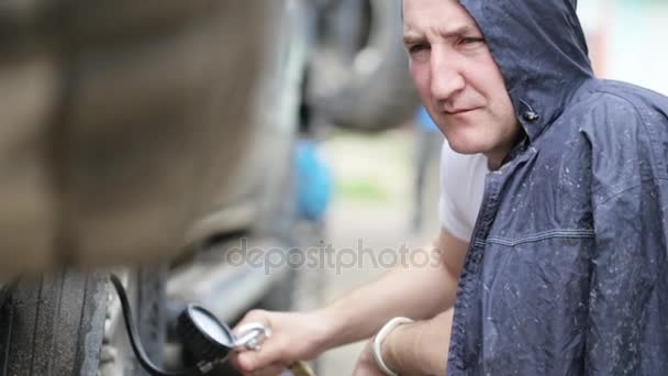 Mann im Regenmantel pumpt Räder von Geländewagen am Straßenrand — Stockvideo