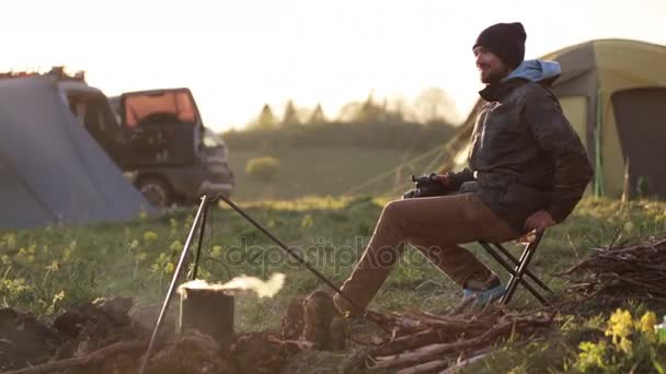 Путешественник, сидящий у костра и фотографирующий на профессиональную камеру . — стоковое видео