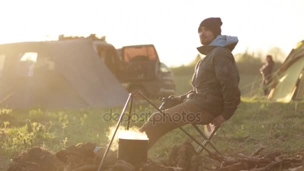 Traveler sitting next to bonfire and taking photo via professional camera. — Stock Video