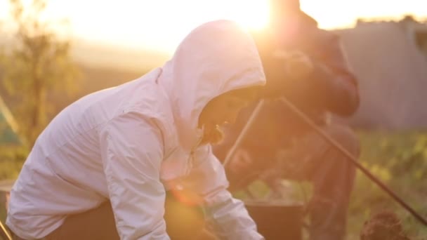 Pareja cocinando la cena en la fogata al atardecer . — Vídeos de Stock