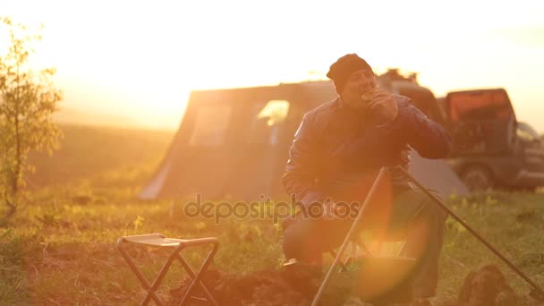 Kaukasische mannen in warme kleren koken diner bij het kampvuur bij zonsondergang. — Stockvideo