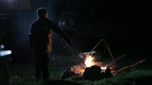 夜晚拍摄到的早午餐在篝火旁边的男孩. — 图库视频影像