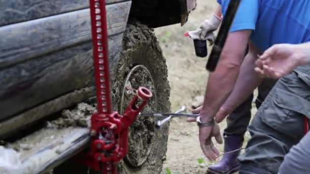 Two travelers replacing wheel of expeditionaty SUV at forest dirty road. — Stock Video