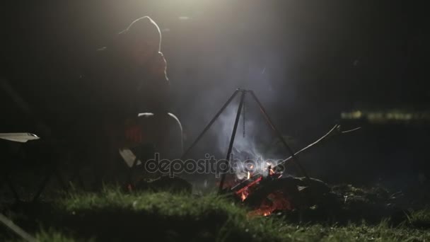 Kaukasier sitzt am Lagerfeuer und telefoniert nachts mit dem Smartphone. — Stockvideo