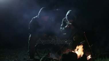 Gece şenlik ateşi yangın yanında oturan ve konuşurken iki arkadaş.