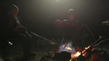 Gece şenlik ateşi yanında oturan, kömür düzeltme ve konuşmak iki erkek.