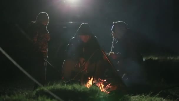 Dos amigos sentados por la noche junto a la hoguera y hablando . — Vídeo de stock