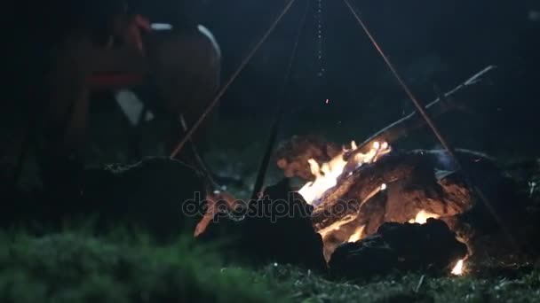 Caucásico hombre sentado al lado de la hoguera y hablando en el teléfono inteligente por la noche . — Vídeo de stock