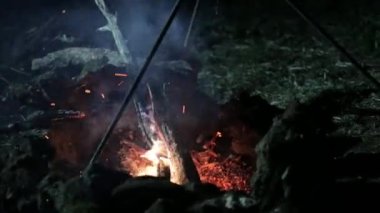 Gece kamp ateşi. Erkek kazanı ateşe koyar..