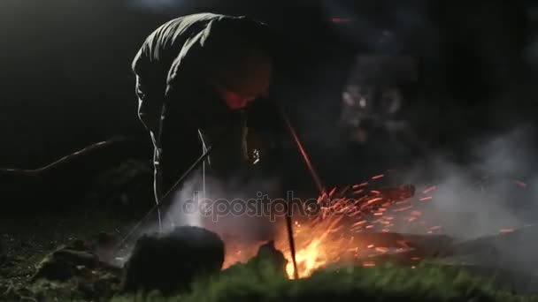 Feu de camp la nuit. Homme ajoutant les bois dans le feu de joie et corrigeant les charbons . — Video