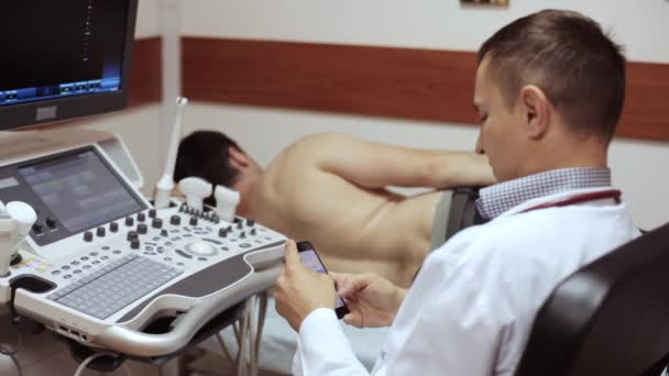 Médico clica telefone inteligente enquanto o paciente deitado e à espera de diagnóstico de ultra-som — Vídeo de Stock