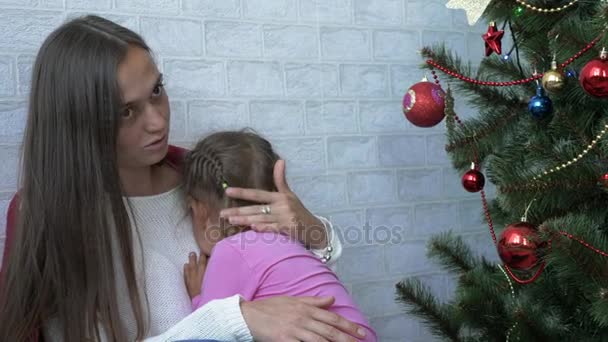 Young mother hugging her crying little daughter next to Christmas tree — Stock Video