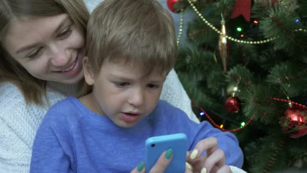 Ευτυχισμένο αγόρι και τη μητέρα της βλέπουν το έξυπνο τηλέφωνο κοντά στο χριστουγεννιάτικο δέντρο — Αρχείο Βίντεο
