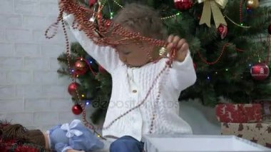 Hediye kutusu ve garland ile oynayan sevimli küçük kız bir şekilde dekore edilmiş Noel ağacı yakınındaki