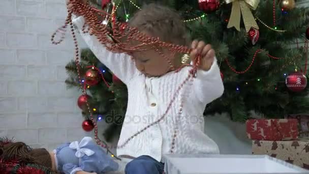 Linda niña jugando con caja de regalo y guirnalda cerca del árbol de Navidad decorado — Vídeos de Stock