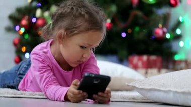 Noel ağacı önünde akıllı telefon kullanan küçük şirin kız. Yakın çekim vurdu.