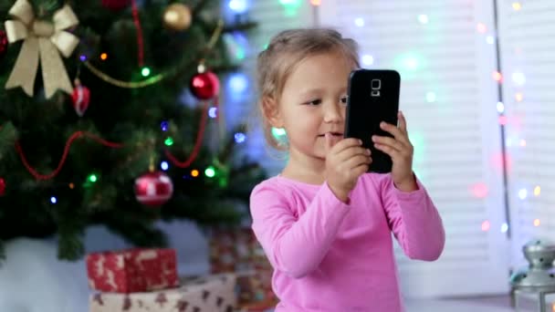 Kleines nettes Mädchen macht Selfie mit Weihnachtsbaum auf dem Hintergrund — Stockvideo