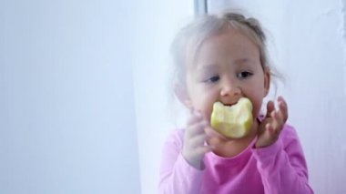 Pencere pervazına ve yeme apple üzerinde oturan sevimli küçük kız portresi.